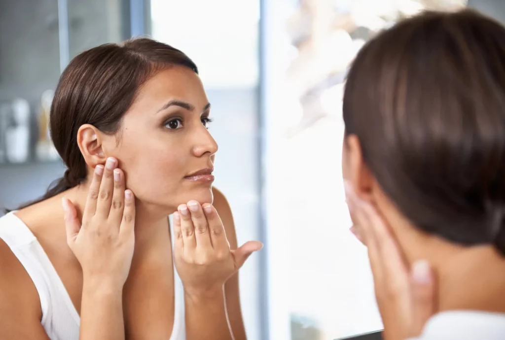 Woman checking her face in mirror after hyperpigmentation treatment in San Mateo