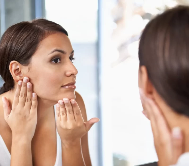 Woman checking her face in mirror after hyperpigmentation treatment in San Mateo